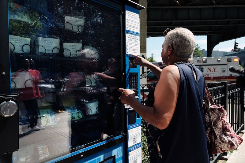 A photo of a woman at a vending machine in Brooklyn that dispenses fentanyl test strips and naloxone as well as hygiene kits, maxi pads, Vitamin C, and COVID-19 tests.