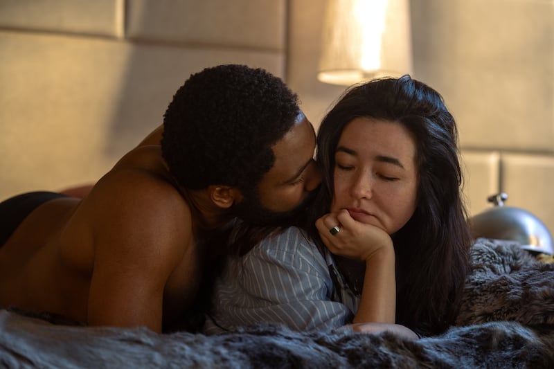 Maya Erskine and Donald Glover lay in bed together in a still from ‘Mr. and Mrs. Smith’