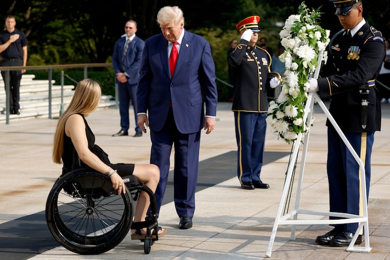 Donald Trump speaks to a woman in a wheelchair in front of a wreath at Arlington National Cemetery