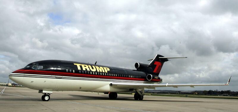 A Boeing 727 on tacam in the livery of Trump, with a white belly, black upper body and gold trimming.