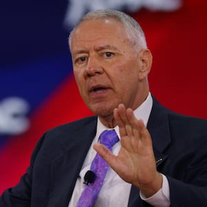 Ken Buck speaks on stage with a hand raised at an event.