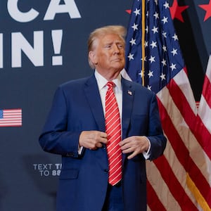 Donald Trump, wearing a red tie and blue jacket, stares forward on stage during an Iowa campaign event.