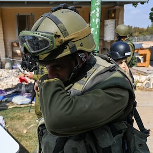 An IDF soldier covering his nose in front of a house.